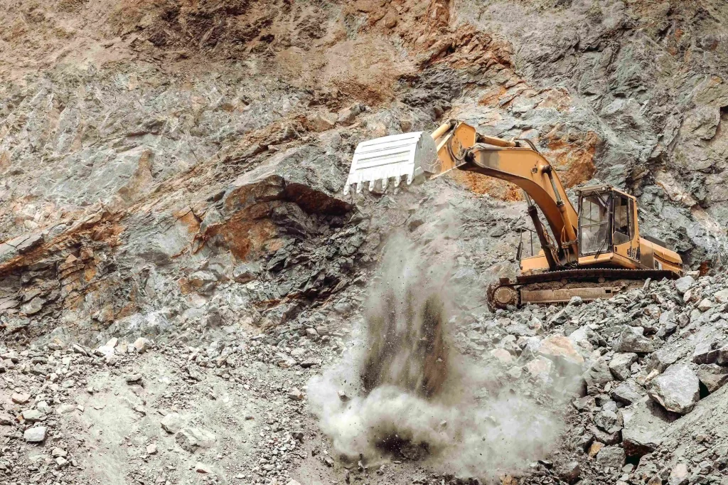 Heavy-duty excavator digging earth in a metal extraction site, with rugged terrain and industrial machinery in operation by Hydrolyz